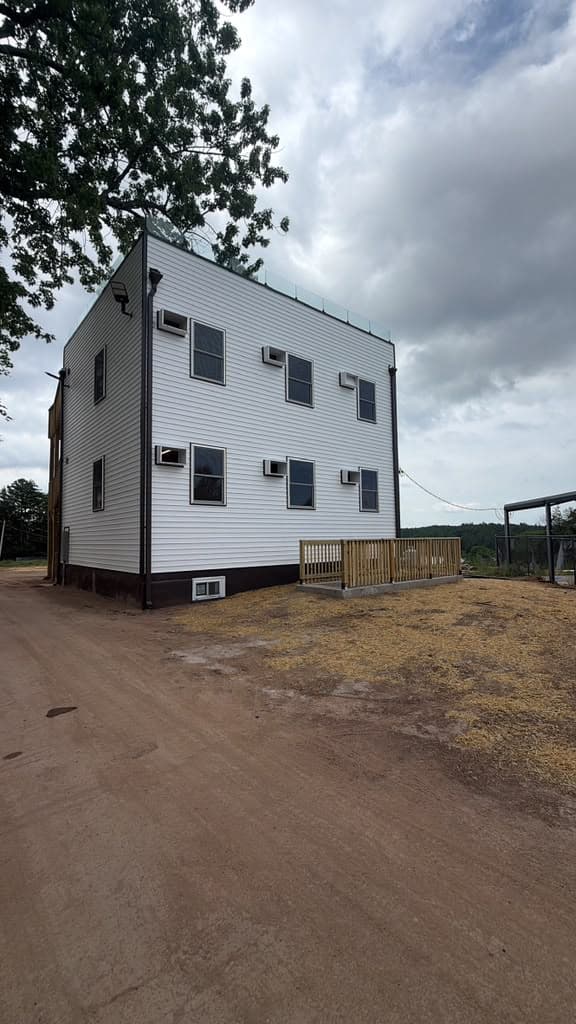 A three-storey sided building on a working site, wall-mounted air handlers on each floor and the ground not yet made good