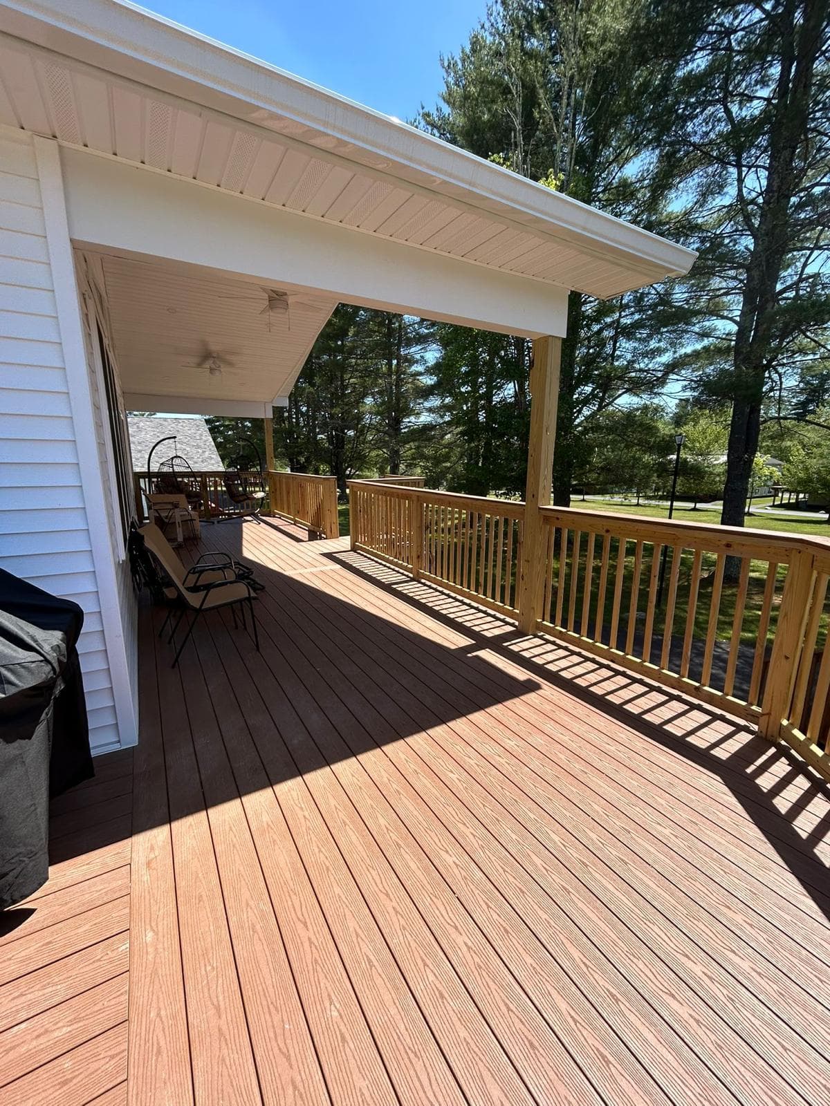 A covered deck running the side of a building — composite boards, a timber balustrade and a panelled porch roof carried on posts, opening to woodland