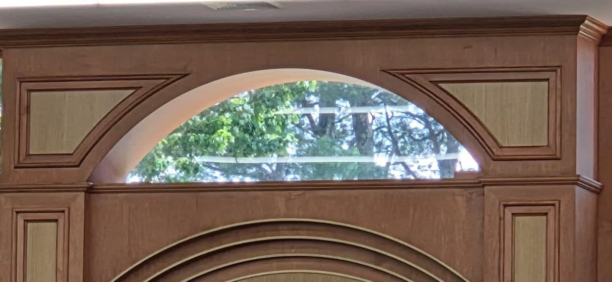 The arched timber surround above an aron kodesh — a moulded arch over a clerestory window, panelled pilasters either side and a deep cornice running above