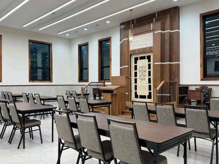 The front of a beis medrash — a panelled timber wall, aron kodesh and amud, with windows down the side wall