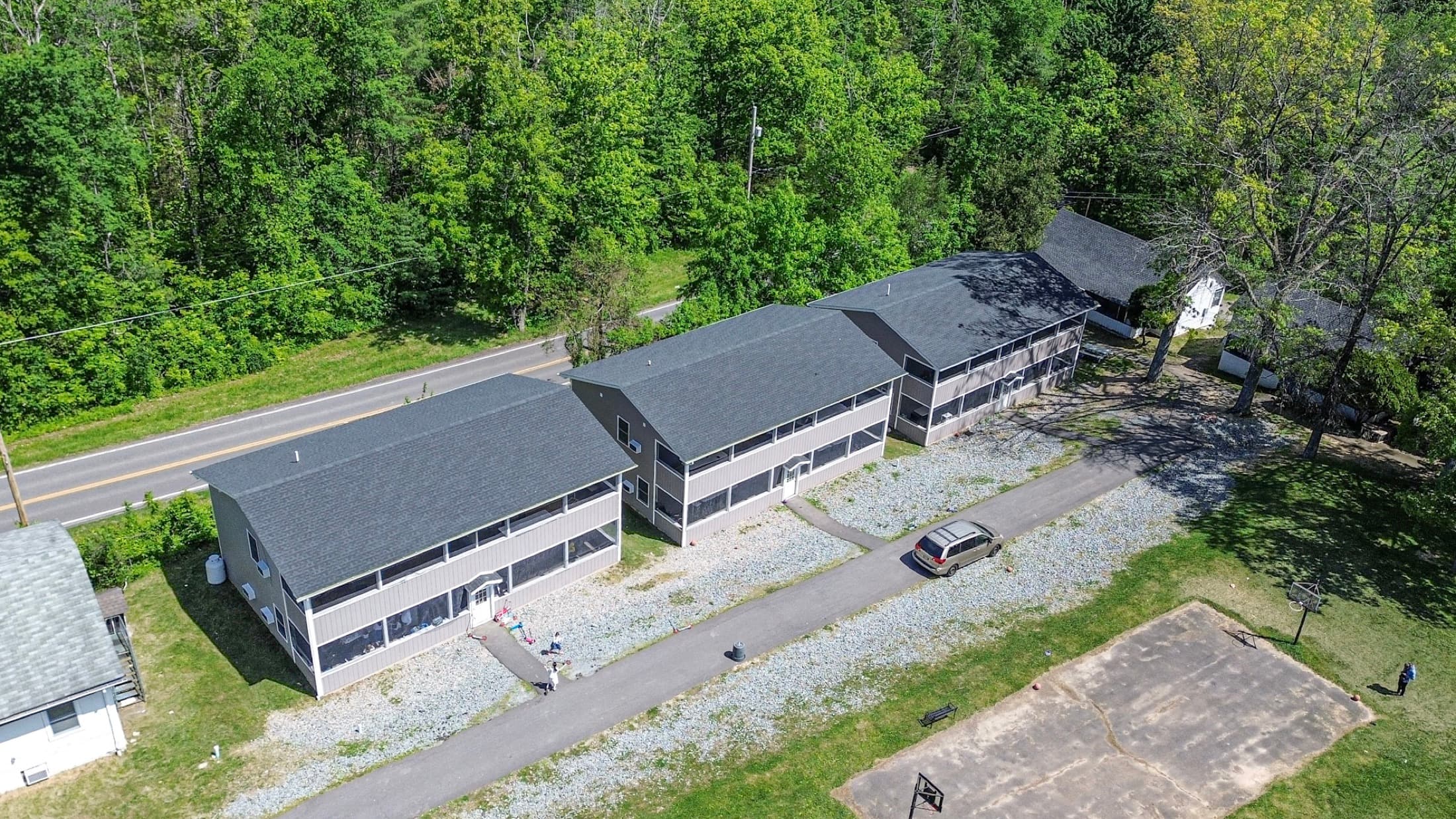 Aerial view of three two-storey buildings with screened porches on both floors, set along a camp road