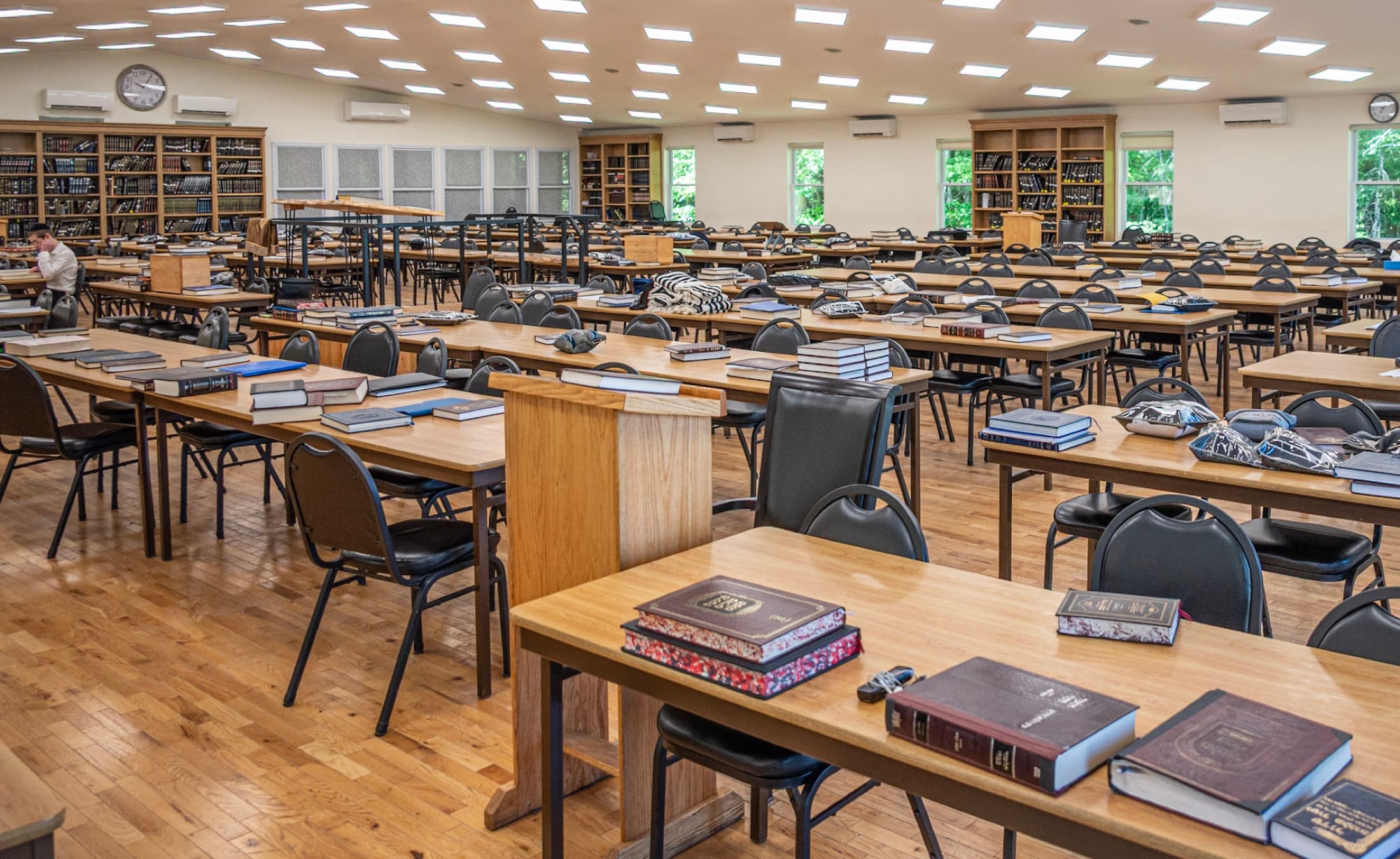 Study tables in a beis medrash with sefarim laid out, wood flooring and no glare on the page