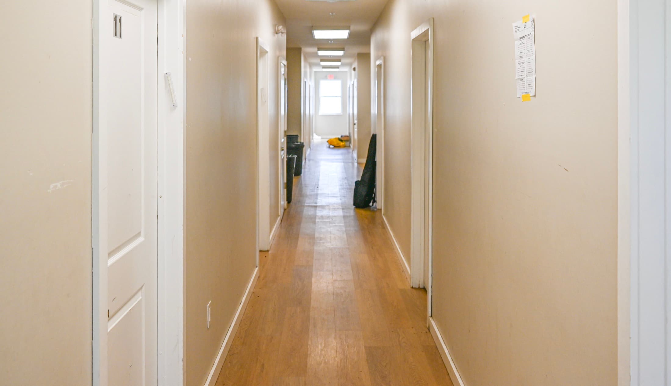 A dormitory corridor running the length of the building past bedroom doors, wood flooring throughout