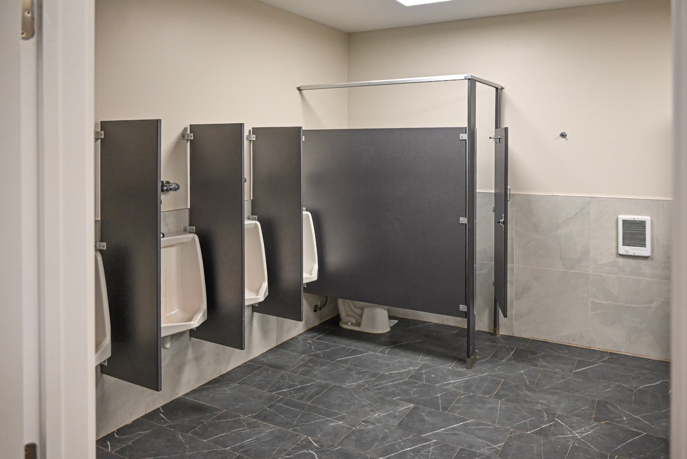A fully tiled camp washroom with urinals and full-height cubicle dividers, built to take constant use