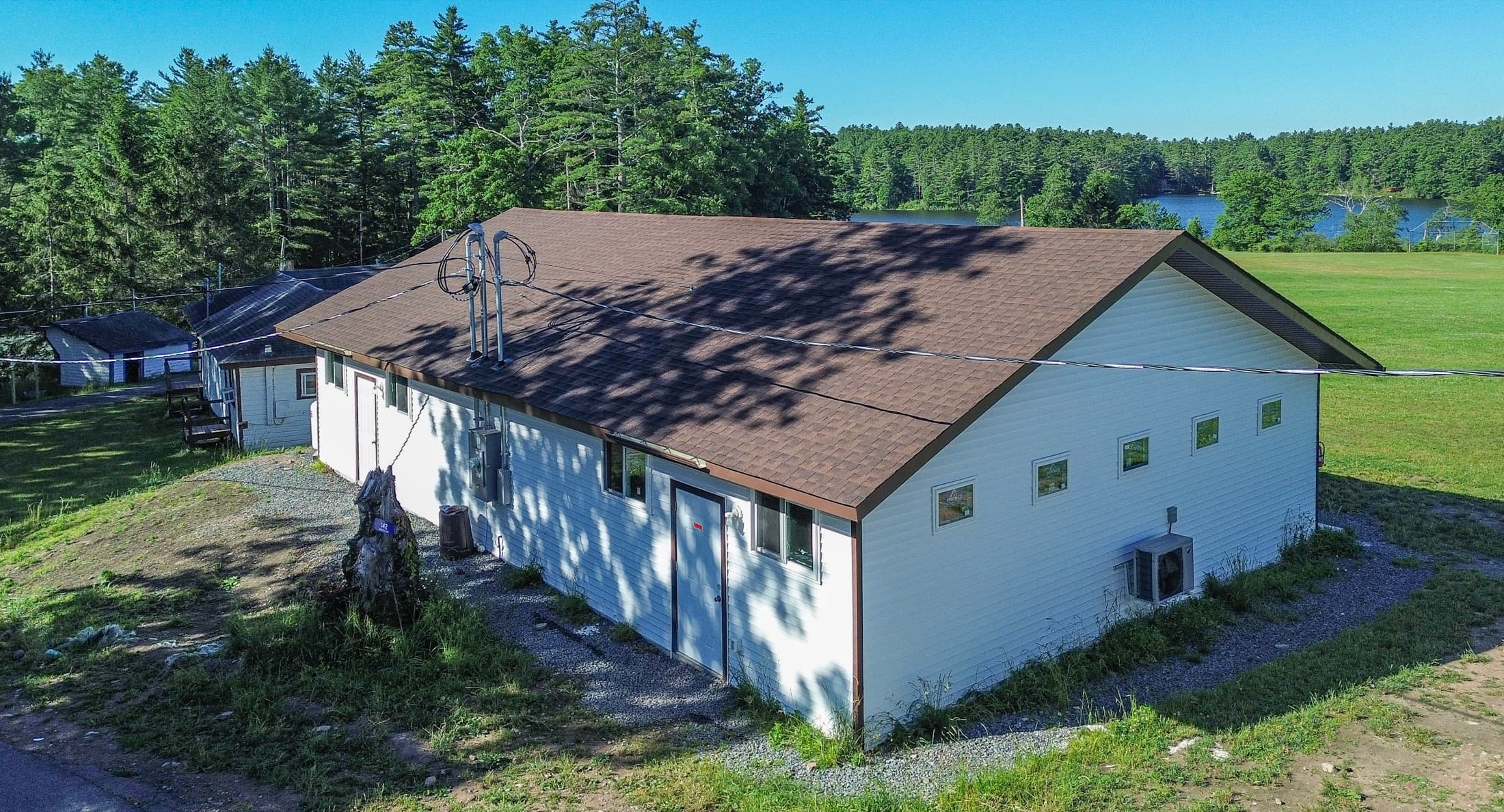 A long single-storey bunk building seen from above, campus fields and lake behind it