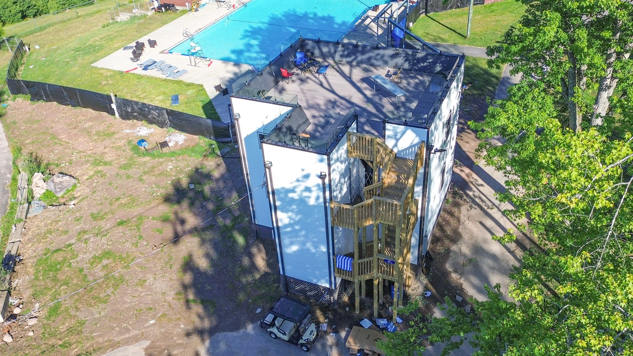 A three-storey dormitory mid-build, one corner still open framing, with the campus pool and fields beyond