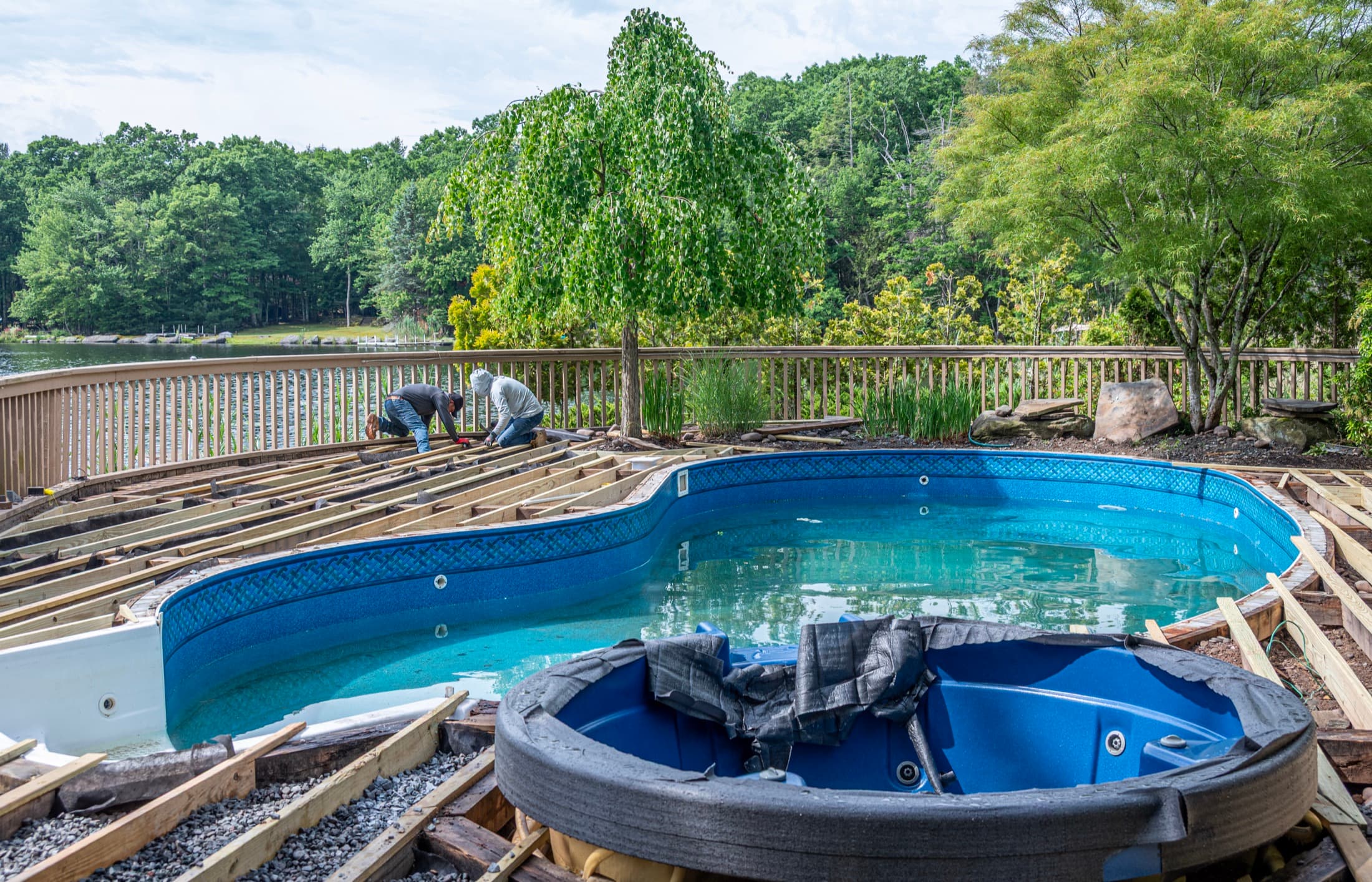 A kidney-shaped pool with a new timber deck wrapping around it, lake beyond the railing